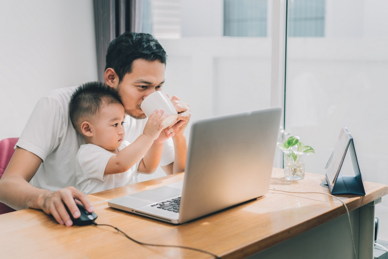 A father looks at a laptop while holding a child on his lap