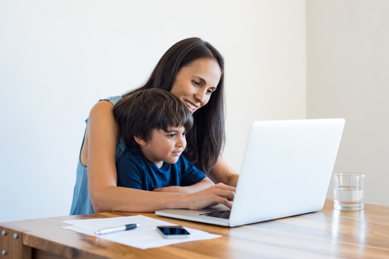 A parent working on her laptop with a young child on her lap